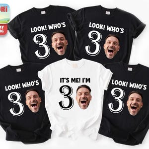 Può includere: Una collezione di magliette nere e bianche. Le magliette nere presentano la scritta "LOOK! WHO'S 30" e il volto di un uomo. Una maglietta bianca dice "IT'S ME! I'M 30". Si tratta probabilmente di magliette per festeggiare il 30° compleanno.