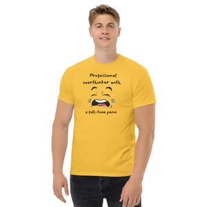 Könnte beinhalten: Senfgelbes T-Shirt mit dem Text "Professional overthinker with a full-time panic" und einer weinenden Gesichts-Grafik. Das T-Shirt hat kurze Ärmel und einen Rundhalsausschnitt.
