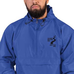 May include: Royal blue Champion windbreaker jacket with a hood and a quarter-zip closure. The jacket features black text that reads "YOU DON'T NEED THEIR PATH. MAKE YOUR OWN." A black graphic of a winding path is also included.
