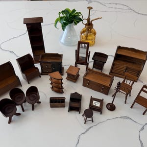 May include: A collection of miniature wooden furniture pieces, including a sofa, chairs, shelves, and cabinets. The furniture is a dark brown color and arranged on a white surface. A small mirror and a plant in a vase are also present.