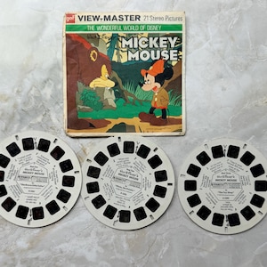 May include: Vintage View-Master set featuring Mickey Mouse. The box art shows Mickey Mouse in a forest scene. Three white View-Master reels are in the foreground. The box reads "The Wonderful World of Disney" and "21 Stereo Pictures."
