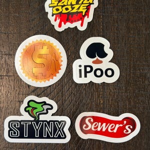 May include: A collection of five stickers with various designs. One sticker reads "SANTA DOZE" in yellow with red dripping accents. Another features a dollar sign. Other stickers include "iPoo", "STYNX", and "Sewer's".