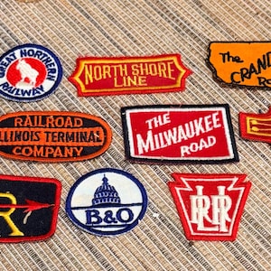 May include: A collection of ten embroidered fabric patches featuring various railroad logos and names including San Francisco Cable Car, Great Northern Railway, North Shore Line, The Crandic Route, Illinois Terminal Company, The Milwaukee Road, Sunset Lines, IR, B&O, and PRR.
