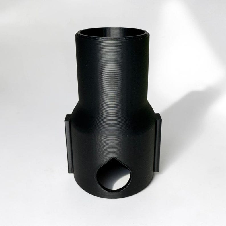 Może przedstawiać: Czarny adapter drukowany w 3D z cylindryczną g&oacute;rą i rozszerzoną podstawą. Adapter posiada otw&oacute;r w kształcie dziurki od klucza i dwa prostokątne boczne przedłużenia. Obiekt jest przeznaczony do konkretnego celu, prawdopodobnie do łączenia lub adaptacji komponent&oacute;w.