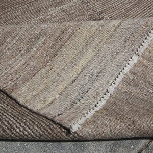 Könnte beinhalten: Nahaufnahme eines gefalteten Teppichs, hauptsächlich beige mit braunen und beigen Akzenten. Die Kanten sind mit einem weißen Fransen versehen. Die gewebte Textur deutet auf ein strapazierfähiges, grobes Material hin.