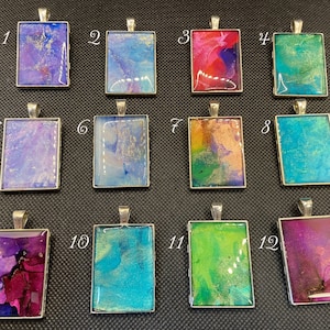 May include: Twelve rectangular resin pendants with silver frames and colorful abstract designs. The pendants are numbered 1 through 12.