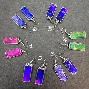 May include: Ten pairs of earrings with different colored resin inlays. The earrings are silver-toned and have a hook closure. The resin inlays are in shades of blue, green, and pink.