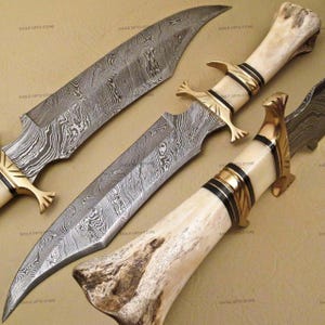 May include: Close-up of three Damascus steel knives with bone handles and brass accents. The blades have a distinctive patterned design. The handles are cream-colored with black and gold bands. The text "EAGLE GIFTS STORE" is visible.