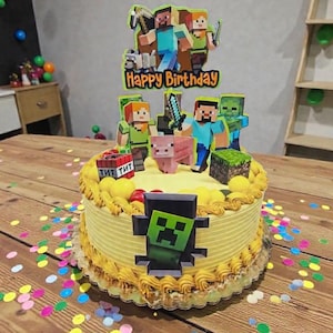 May include: A yellow frosted birthday cake decorated with Minecraft character toppers and a Creeper face. The cake has a "Happy Birthday" sign and is surrounded by colorful confetti on a wooden table.