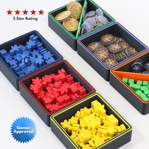 Puede incluir: Organizador de juegos negro con múltiples compartimentos, cada uno con diferentes piezas de juego. Las piezas son de varios colores, incluyendo azul, rojo, amarillo y verde. El organizador también contiene monedas de juego. El texto en la imagen dice "5 Star Rating" y "Gamer Approved."