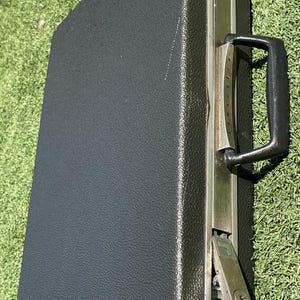 Puede incluir: Un maletín rígido de color negro con exterior texturizado, asa de plástico negro y cierres metálicos plateados. El borde metálico presenta la marca Samsonite grabada verticalmente junto al asa e incluye dos cerraduras con llave.