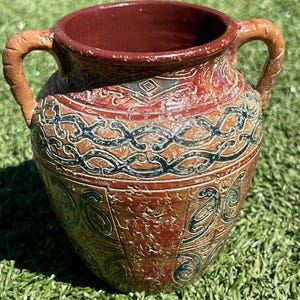 May include: A brown ceramic vase with two handles. The vase has a textured surface with intricate patterns in black and blue. The rim and interior are a darker shade of brown.