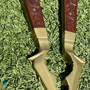 May include: Vintage nutcracker with a brass and wood design. The handles are dark brown with carved floral patterns and brass accents. The nutcracker's jaws are made of brass.