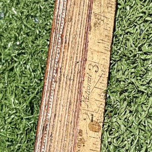 May include: A vintage wooden folding ruler with metal hinges. The ruler is marked with inch measurements and the text "National". The ruler is lying on a bed of green grass.