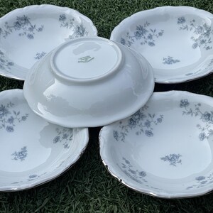 May include: A set of five white porcelain bowls with a floral pattern in blue. The bowls have a scalloped edge with a silver trim. The bowls are arranged on a green surface.