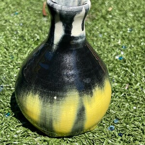 May include: A handcrafted ceramic vase with a unique color gradient. The vase transitions from a yellow base to a black midsection, culminating in a dark blue and white rim. The vase is a decorative item.