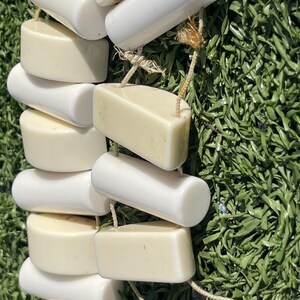 May include: A strand of off-white and white ceramic beads, strung together with natural twine. The beads are cylindrical and rectangular, with rounded edges. The background is artificial green turf.