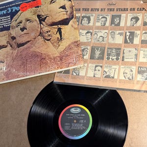 May include: A collection of vintage vinyl records. One album cover features Mount Rushmore with the text "Score 3 Points". Another shows a collage of album covers. A black vinyl record is visible.