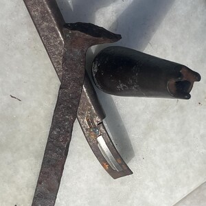 May include: A collection of vintage metal tools, including a nail puller, a nail, and a cylindrical object. The tools are heavily rusted, with visible wear and tear. The nail puller has a curved blade and a handle. The nail is long and rectangular. The cylindrical object has a hole.