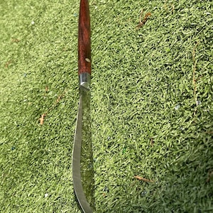 May include: A curved, stainless steel knife with a dark brown wooden handle. The blade has a slight curve and a sharp edge. The handle is a rich, dark brown color, and the knife appears to be well-crafted.