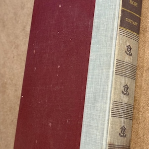 May include: A hardcover book titled "The Black Rose" by Costain. The book has a burgundy cover and a light blue spine. The spine features the title and author's name in gold lettering, with decorative elements.