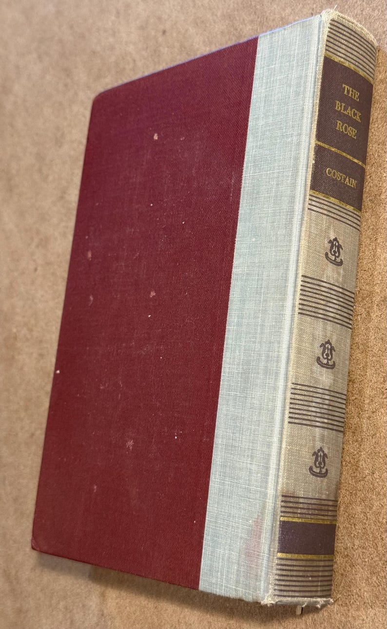 May include: A hardcover book titled "The Black Rose" by Costain. The book has a burgundy cover and a light blue spine. The spine features the title and author's name in gold lettering, with decorative elements.