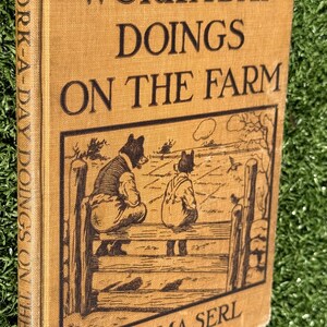 May include: Antique book titled "WORK-A-DAY DOINGS ON THE FARM" by Emma Serl. The cover is tan with black lettering and a black and white illustration of two figures on a fence. The book's spine also has the title printed vertically.