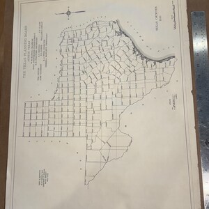 May include: A vintage map of Texas counties, with the title "The Texas Planning Board" and the city of Austin, Texas. The map is printed in black ink on aged paper, with a scale of 200. A ruler is visible on the right side.