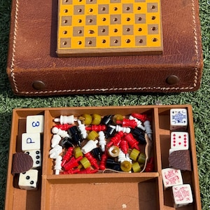 May include: A vintage travel game set with a brown leather case. The set includes a yellow and brown game board, dice, and various game pieces in red, black, white, and green. The set is designed for travel and compact storage.