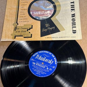 May include: A vintage vinyl record album titled "Music Treasures of the World" featuring Tchaikovsky's "The Nutcracker." The album cover is tan and gold with text and a key graphic. The record is black with a blue label.