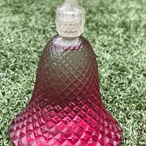 May include: A decorative bell-shaped glass bottle with a diamond pattern. The bottle transitions from clear to a deep pink hue. It features a clear, textured stopper, adding a touch of elegance. This vintage-style bottle is ideal for display or as a unique decorative piece.