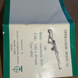 May include: An open operation manual with a green border. The manual features text including "Semi-Automatic Rifle" and "CAL. 7.62 x 39 mm." A line drawing of a rifle is also visible. The manufacturer is MAADI Co. For Engineering Industries.