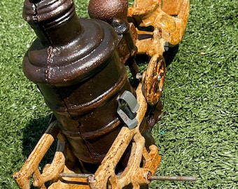 May include: A vintage, cast-iron cannon model with a brown finish. The cannon features an eagle emblem and is mounted on a weathered, tan carriage with wheels. The cannon is set against a green background.