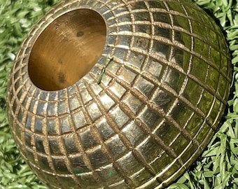 May include: A dome-shaped brass candle holder featuring a textured grid pattern across its exterior surface. The object has a circular opening at the top and a smooth, polished metallic finish that reflects light across its geometric surface.