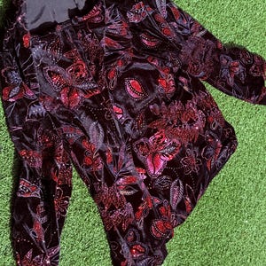 May include: Black velvet top with a floral pattern in shades of red and pink. The long-sleeved top features a square neckline and is embellished with sequins. The floral design includes leaves and paisley shapes.
