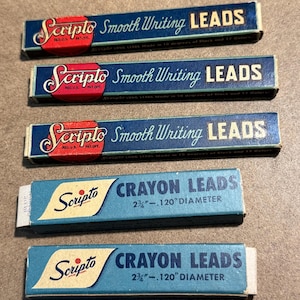 May include: A collection of vintage Scripto lead boxes. The boxes are primarily blue with red and white accents. The text on the boxes reads "Scripto Smooth Writing LEADS" and "Scripto CRAYON LEADS". The crayon leads are 2.75 inches in length.