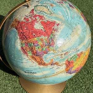 May include: A vintage Replogle World Nation globe with a gold-coloured base and meridian. The globe features a detailed map with various colours representing different countries and regions. The globe is set against a green background.