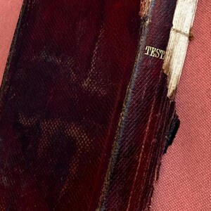 May include: A vintage, burgundy-colored book with a textured, patterned cover. The spine displays the gold-lettered word "TEST". The book shows signs of age and wear, with distressed edges and a worn appearance.
