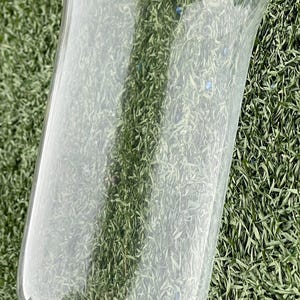 May include: A clear glass hurricane candle holder with a flared top and a rectangular base. The glass is smooth and transparent, allowing light to pass through. The holder is designed to protect candles from wind.