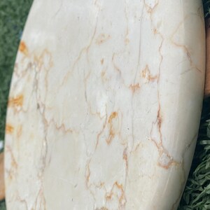 May include: Oval-shaped, polished stone with a creamy white base and intricate brown veining. The natural stone has a smooth, glossy finish, showcasing the unique patterns of the mineral. The stone is likely used for decorative purposes.