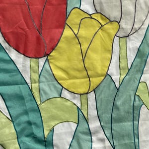 May include: A fabric floral design featuring red, yellow, and white tulips with green leaves and stems. The flowers are outlined in black against a white background. The tulips are in a purple pot.
