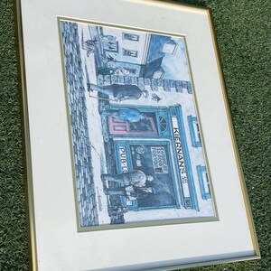 May include: Framed print of a pub scene with figures outside. The pub's sign reads "Kiernan's Pub" and "Guinness is good for you." The artwork is in a gold frame with a white mat, set against a green background.