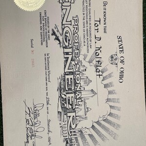May include: A vintage certificate from the State of Ohio, issued to Tor D. Kolflat, a Professional Engineer. The document features ornate lettering, a gold seal, and a detailed illustration of a cityscape. Dated March 27th, 1964.