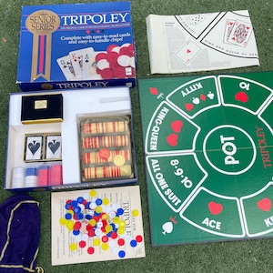 May include: A vintage Tripoley board game set, featuring a blue box with the game title and cards. The set includes a green game board, playing cards, chips, and a dice. The game is designed for easy reading and handling.