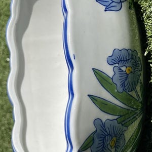 May include: White ceramic planter with a scalloped edge, adorned with blue floral designs and green leaves. The rim is trimmed with a blue stripe. The planter is approximately 12 inches long.