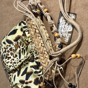 May include: A handmade bag with a woven straw front and a leopard print fabric pouch. The bag features a macrame strap with wooden and black beads. A tag with the text "Sani Natural Acc." is attached.