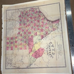 May include: A vintage map of Texas, featuring pink and yellow shaded areas, with the title "Pocket Map STATE TEXAS 1879." The map shows the state's outline and geographical features. A ruler is placed on the right side of the map.