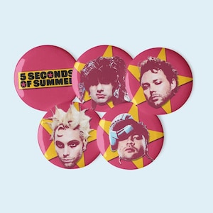 Op de afbeelding: Een verzameling van vijf ronde, bordeauxrode buttons met afbeeldingen van bandleden. Elke button heeft een gele sterrenburst-achtergrond. Eén button toont de tekst "5 SECONDS OF SUMMER" in geel en wit.