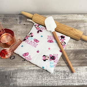 May include: A collection of kitchen tools including copper measuring cups and spoons, a wooden rolling pin, a white spatula, and a Valentine's Day themed pot holder with Minnie Mouse graphics and the text "Be My Valentine."