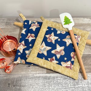 May include: A collection of kitchen items including copper measuring cups and spoons, two navy blue pot holders with star and gingerbread man patterns, and a spatula with a green Christmas tree design.